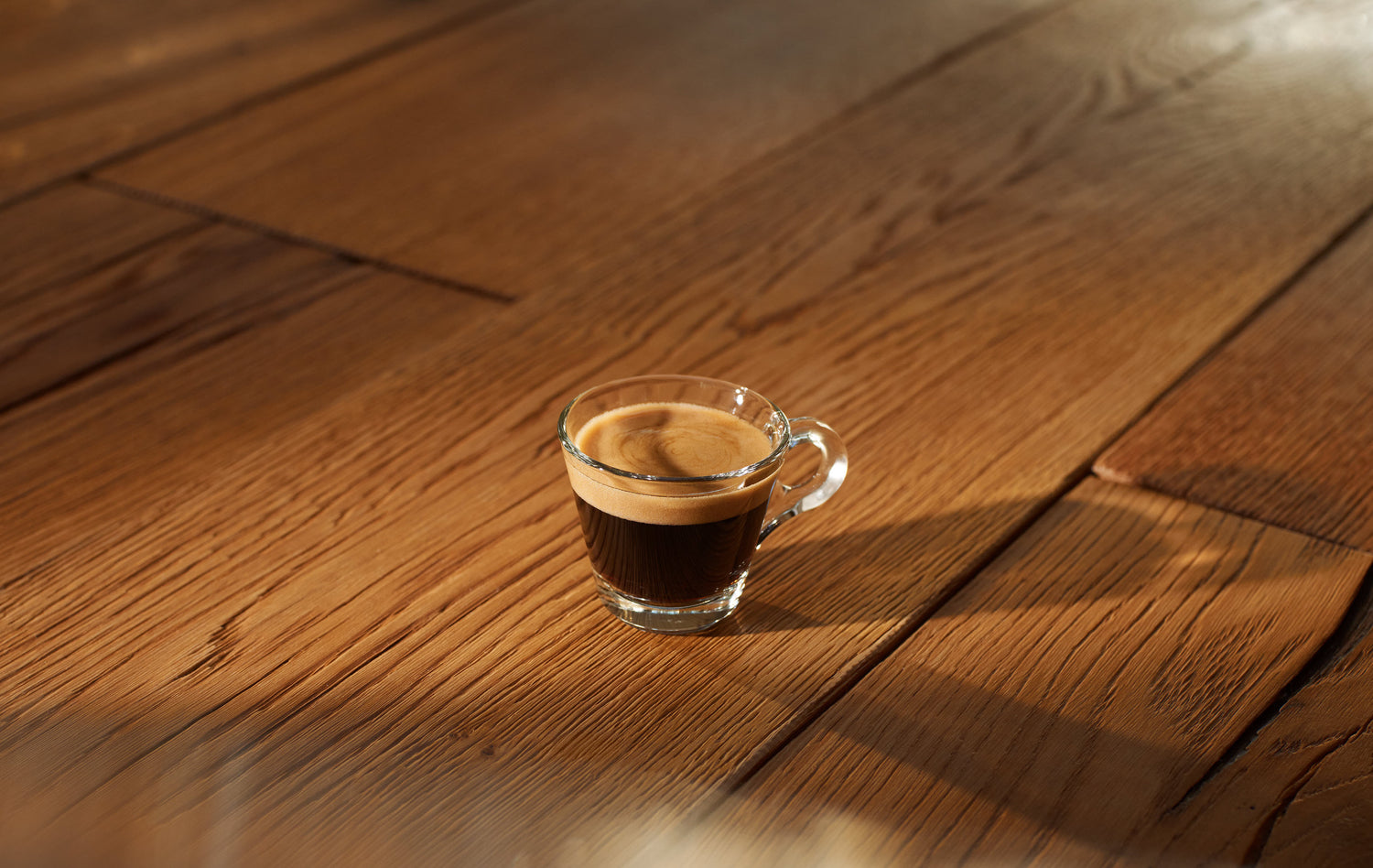 Eine Glastasse mit Espresso auf einem Holztisch.