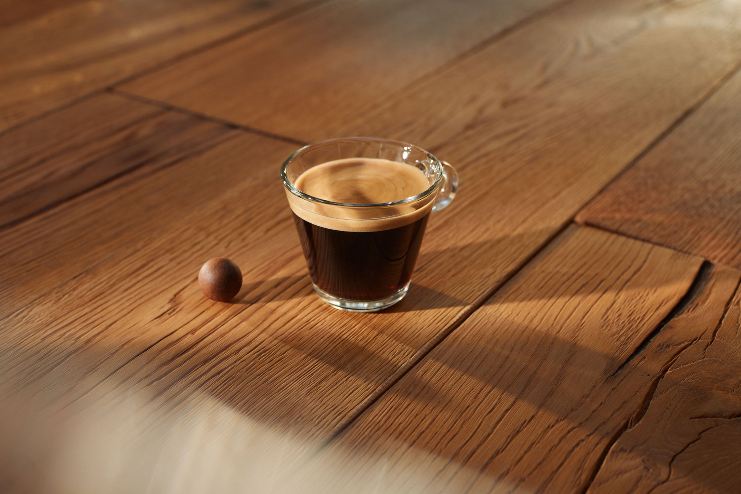 Eine Glastasse mit Kaffee, daneben ein Coffee Ball.